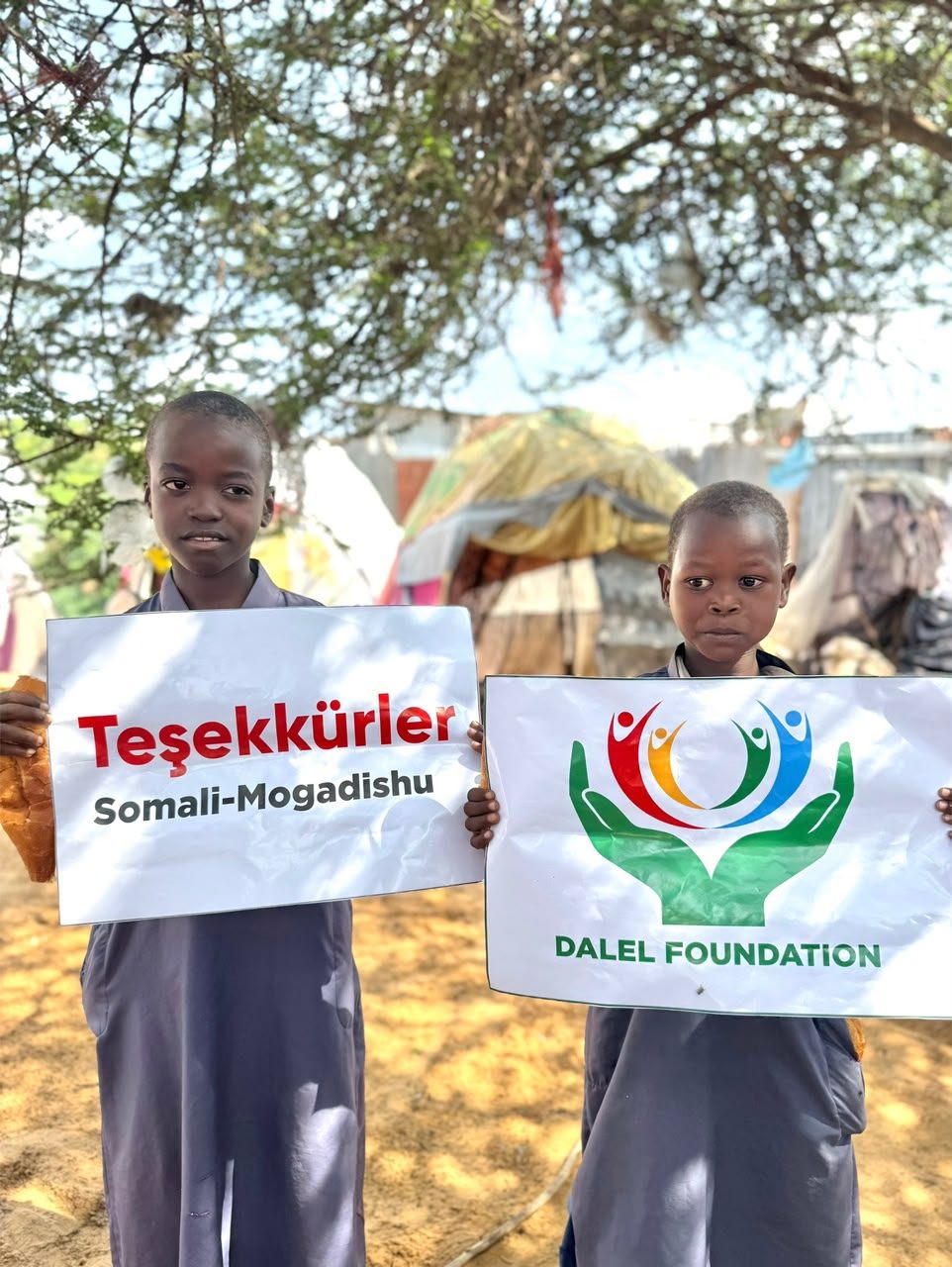 Two children holding bread and signs bearing the Dalel Foundation logo and a thank you message from Mogadishu