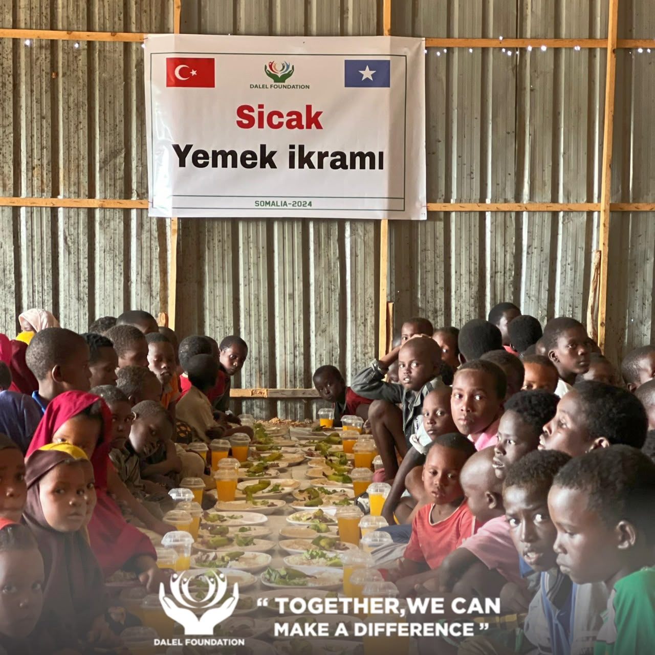 Children seated together at a long spread of hot meals and drinks at a Dalel Foundation food distribution