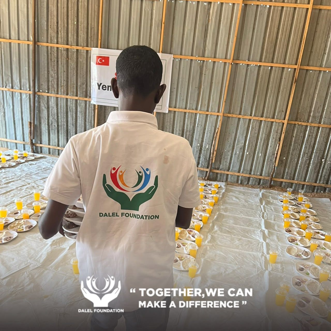 A Dalel Foundation volunteer carrying a stack of plates across a hall set for a hot meal service