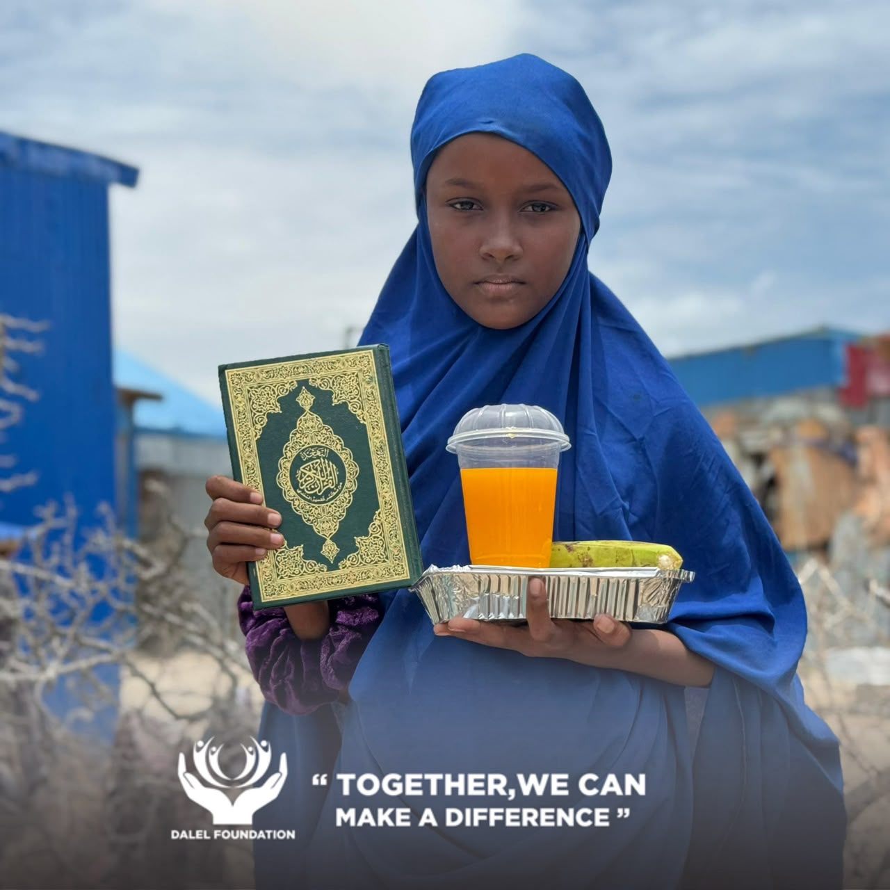 A girl in a blue headscarf holding up her Qur'an beside a tray of food and fresh juice