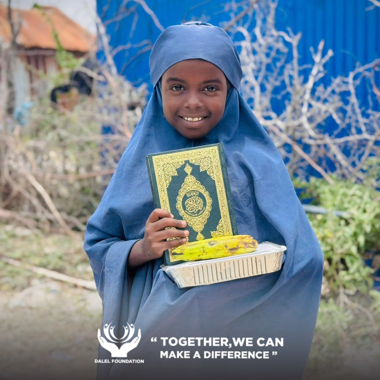 A smiling girl in a blue headscarf holding her Qur'an and a tray of food