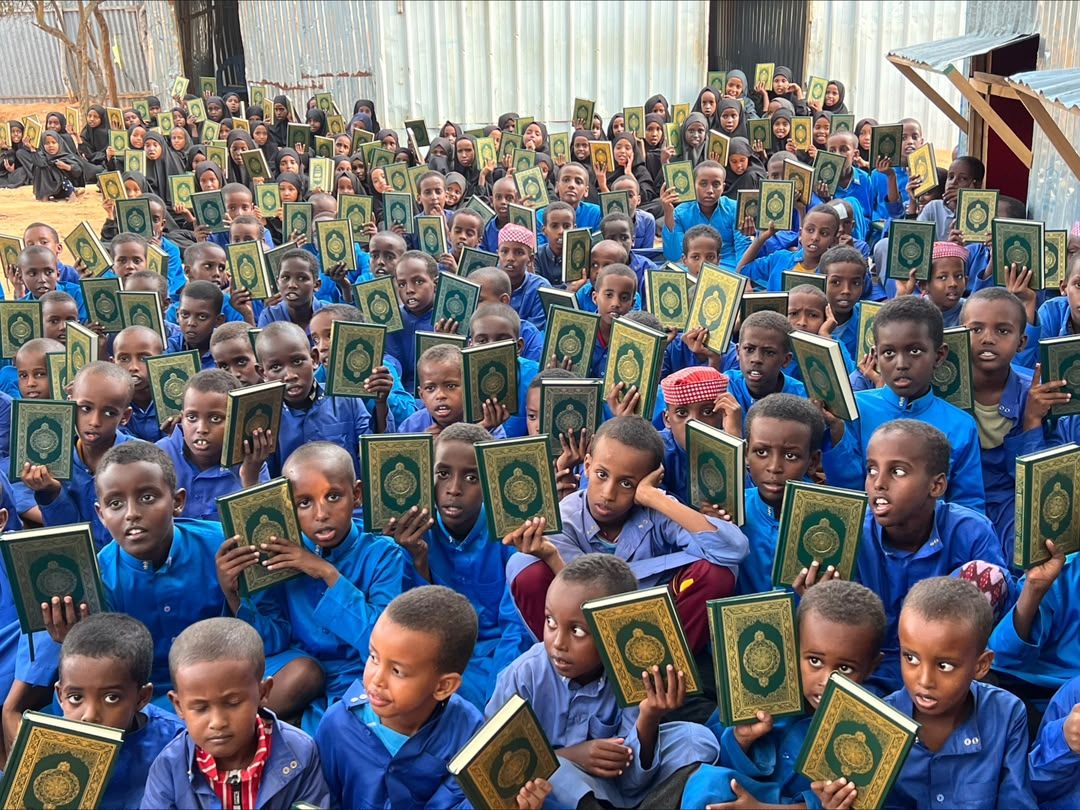 Qur'an students in blue uniforms holding up copies of the Qur'an provided by Dalel Foundation