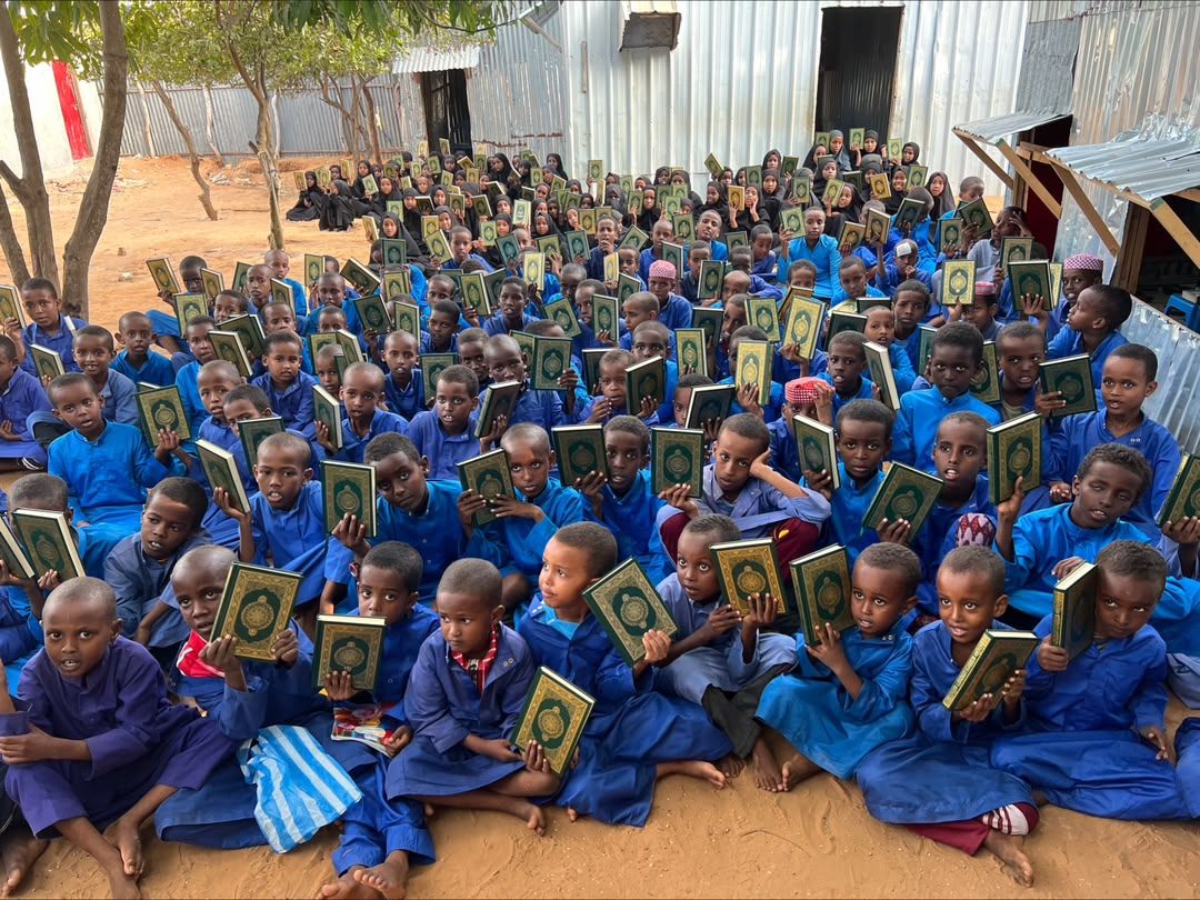 A large group of Qur'an students seated outdoors holding up their Qur'ans